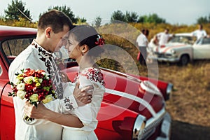 Stylish bride and happy groom near car on the background of nature and friends bridesmaids