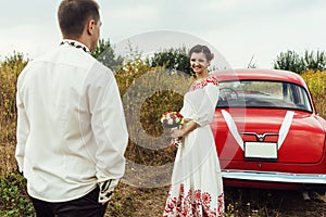 Stylish bride and happy groom near red retro car on the background of nature