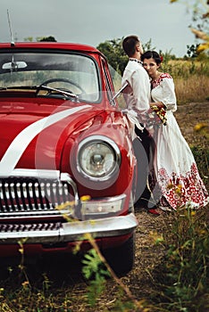 Stylish bride and happy groom near red retro car on the background of nature