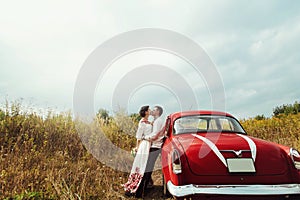 Stylish bride and happy groom near red retro car on the background of nature