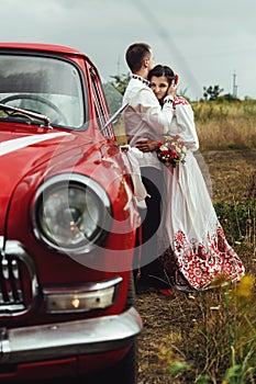 Stylish bride and happy groom near red retro car on the background of nature