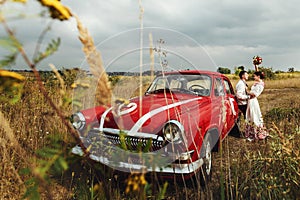 Stylish bride and happy groom near red retro car on the background of nature