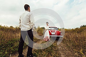 Stylish bride and happy groom near red retro car on the background of nature