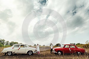 Stylish bride and happy groom near  two retro cars on the background of nature