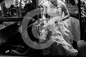 Stylish bride in vintage white wedding dress getting into black limousine with groom, happy couple sitting in car before wedding