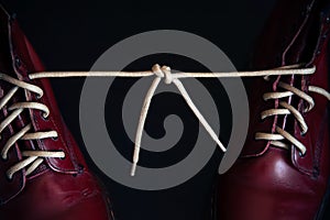 Stylish bright red shoes with thick white laces tied together, close-up, selective focus, space for text. April Fools` day, prank