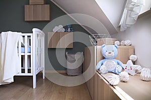 Stylish and bright scandinavian decor of newborn baby room with white design furnitures, natural toys, accessories and teddy bears