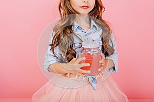 Stylish brightful image of cute little girl with long brunette hair, in tulle skirt holding glass with juice  on