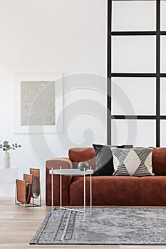 Stylish brown corner sofa with patterned pillows in elegant living room interior with mullions wall