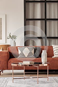 Stylish brown corner sofa with patterned pillows in elegant living room interior with mullions wall