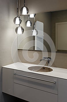 Stylish brown sink, chrome faucet, large mirror and ceiling light three-lamp chandelier. Modern bathroom design