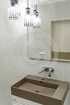 Stylish brown sink, chrome faucet, large mirror and ceiling light three-lamp chandelier. Modern bathroom design