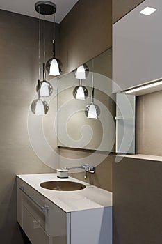 Stylish brown sink, chrome faucet, large mirror and ceiling light three-lamp chandelier. Modern bathroom design