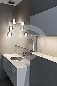 Stylish brown sink, chrome faucet, large mirror and ceiling light three-lamp chandelier. Modern bathroom design