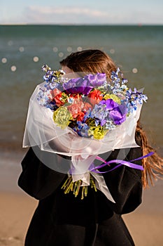 Stylish brunette woman in black coat hides by bright flower arragement