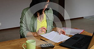 Stylish brunette woman in glasses sitting at wooden table with notepad working in her office