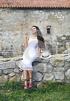 Stylish brunette woman in white dress on background of brick wall