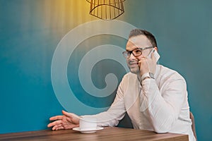 Stylish business European businessman in glasses and white shirt talking on a smartphone sitting at a table in a cafe on a break