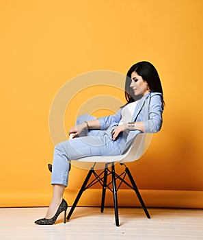 Stylish business woman  brunette in blue official suit and high-heeled shoes sitting in designer armchair looking down