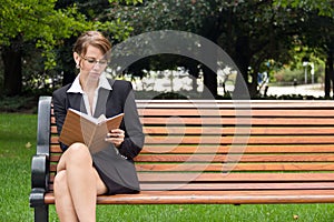 Stylish business woman siting on park bench writing in notebook