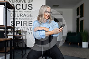 stylish business woman sitting on a chair with a phone in her hands in the middle of the office