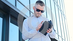 A stylish businessman is counting money in his wallet, he is wearing a blue shirt and sunglasses