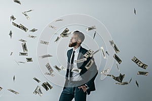 Stylish businessman with falling dollar banknotes on grey