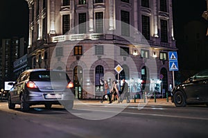 A stylish businesspeople enjoys an evening stroll on a city street, illuminated by the lights of a grand historic