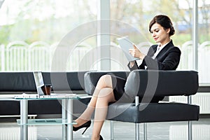 Stylish businesswoman sitting on sofa using tablet pc in the office.