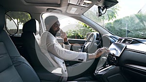 Stylish buzy african american businessman sitting in the driver`s seat ,talking on phone and tuning the car on the