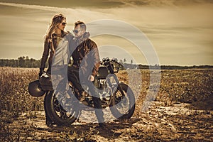 Stylish cafe racer couple on the vintage custom motorcycles in a field.