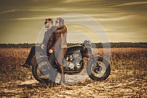 Stylish cafe racer couple on the vintage custom motorcycles in a field.