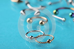 Stylish captive bead rings on light blue background, closeup. Piercing jewelry