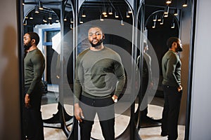 Stylish casual african american man at fitting room clothes store, looking on mirror. The concept of stylish men`s clothing