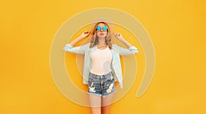 Stylish caucasian blonde young woman posing wearing straw hat, shorts and shirt on yellow background