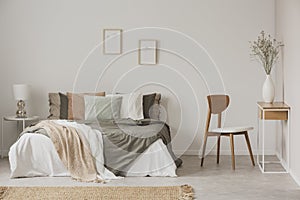 Stylish chair next to warm king size bed in scandinavian bedroom