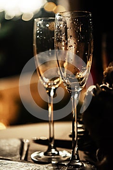 Stylish champagne glasses empty on background of warm romantic candle light at evening wedding ceremony