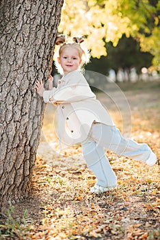 Stylish child girl 4-5 year old lean on tree wear jacket and denim pants in park outdoor.