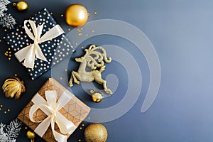 Stylish Christmas background with gift boxes, gold baubles decoration and reindeer on dark blue table. Flat lay, top view
