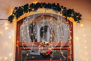 Stylish christmas decorations, garland lights, modern wreath, fir branches with ornaments on window of cafe in european city