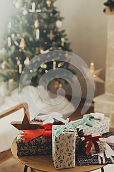 Stylish christmas gifts in festive wrapping paper with bows and vintage ornaments on wooden table on background of golden