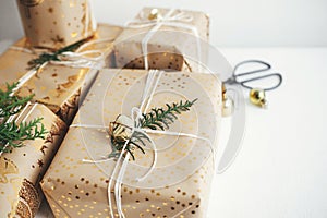 Stylish christmas gifts. Modern christmas gift boxes with fir branch, golden bell, festive paper and ornaments composition on