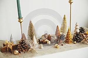 Stylish christmas golden trees, runner with gold stars, shiny baubles and candles on table. Modern gold christmas decorations.