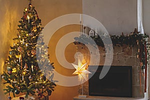 Stylish christmas living room with modern decorated christmas tree and festive decor on fireplace mantel with golden light.