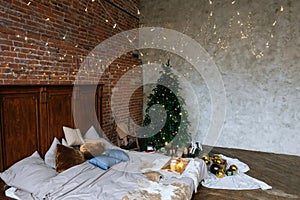 Stylish Christmas loft interior,cozy bedroom with wooden bed and a lot of lights with a decorated Christmas tree and a