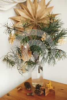 Stylish christmas star straw ornaments and paper angel on pine branches on table in vase on background sweden star. Festive