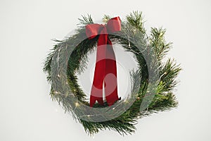 Stylish christmas wreath with red bow and golden lights hanging on white wall. Merry Christmas and Happy Holidays! Simple