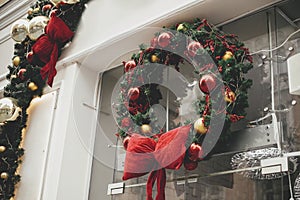 Stylish christmas wreath with red and gold baubles and big bow on window store or building facade. Modern Christmas festive decor