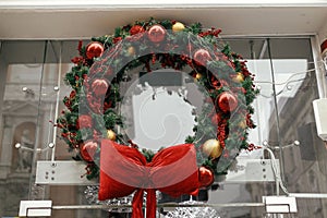 Stylish christmas wreath with red and gold baubles and big bow on window store or building facade. Modern Christmas festive decor