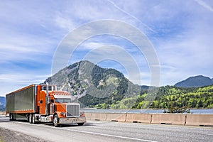 Stylish classic orange big rig semi truck bonnet tractor with same color reefer semi trailer trim and refrigerator unit